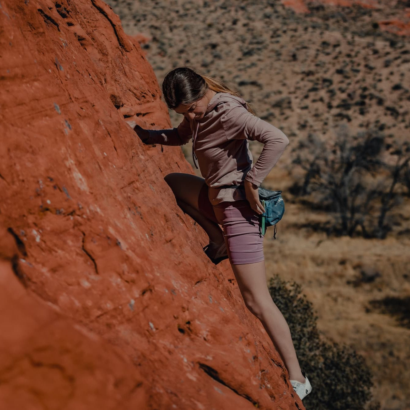 a woman bouldering wearing a pink Solstice Merino Wool Sun Hoodie