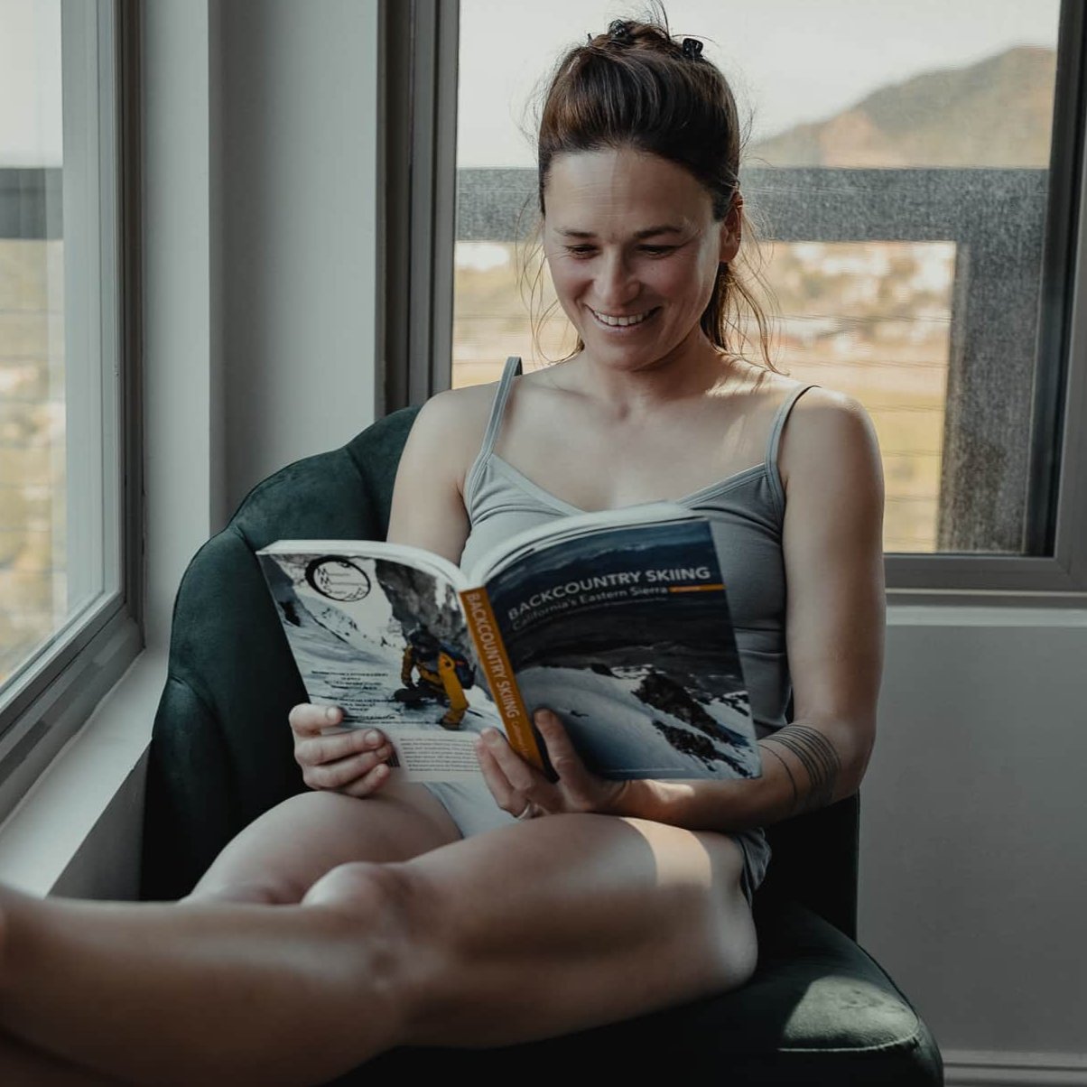 A woman looking at a Backcountry Skiing guide book wearing a Ridge cami tank